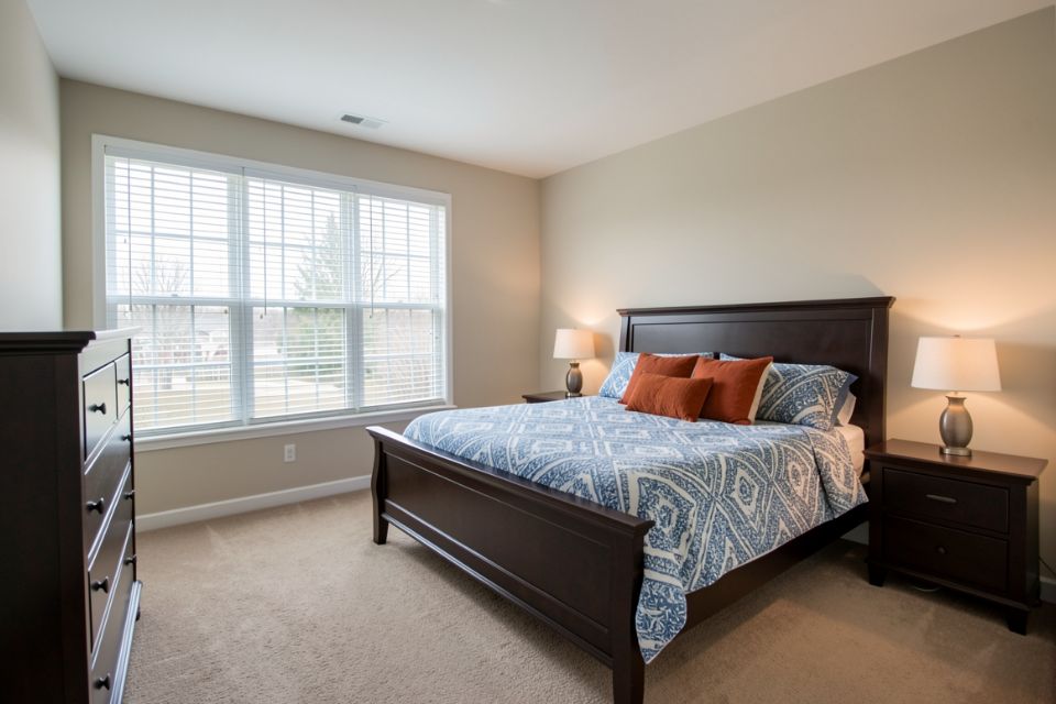 A condominium bedroom with a dark wood bed, a blue and white duvet and a wide window.