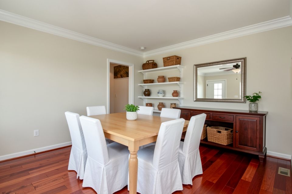 A condominium dining area with a light oak table, white slipcovered chairs and open shelves.