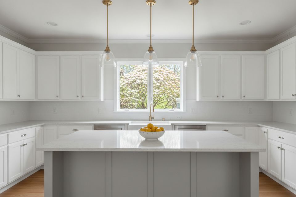 A staged kitchen with white shaker cabinets, a gray quartz island and a bowl of lemons.