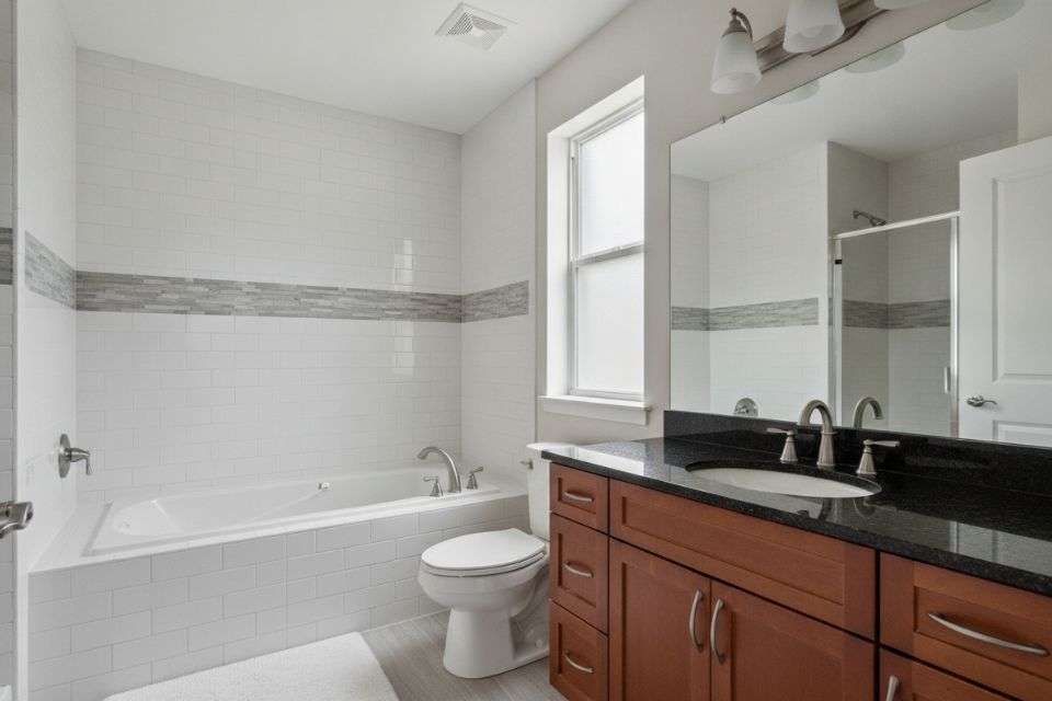 A condominium bathroom with a white tile tub surround and a cherry vanity.