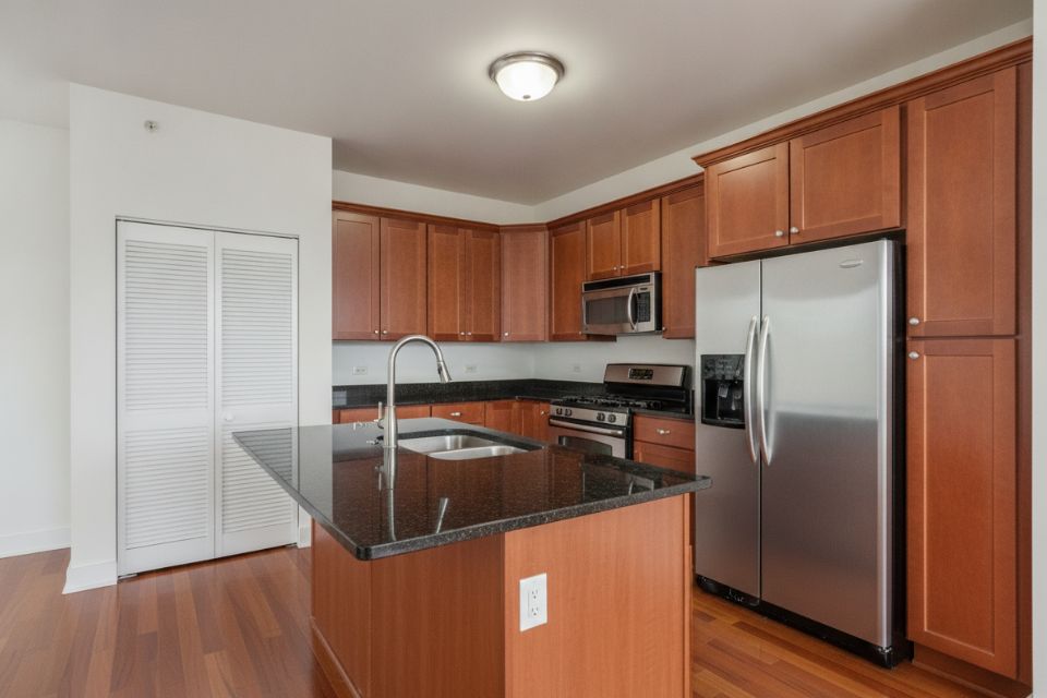 A condominium kitchen with a black granite island, cherry cabinets and stainless appliances.