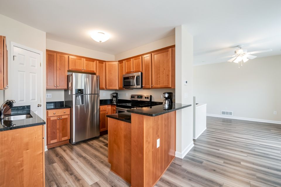 An open condominium kitchen with cherry cabinets, black granite counters and stainless appliances.